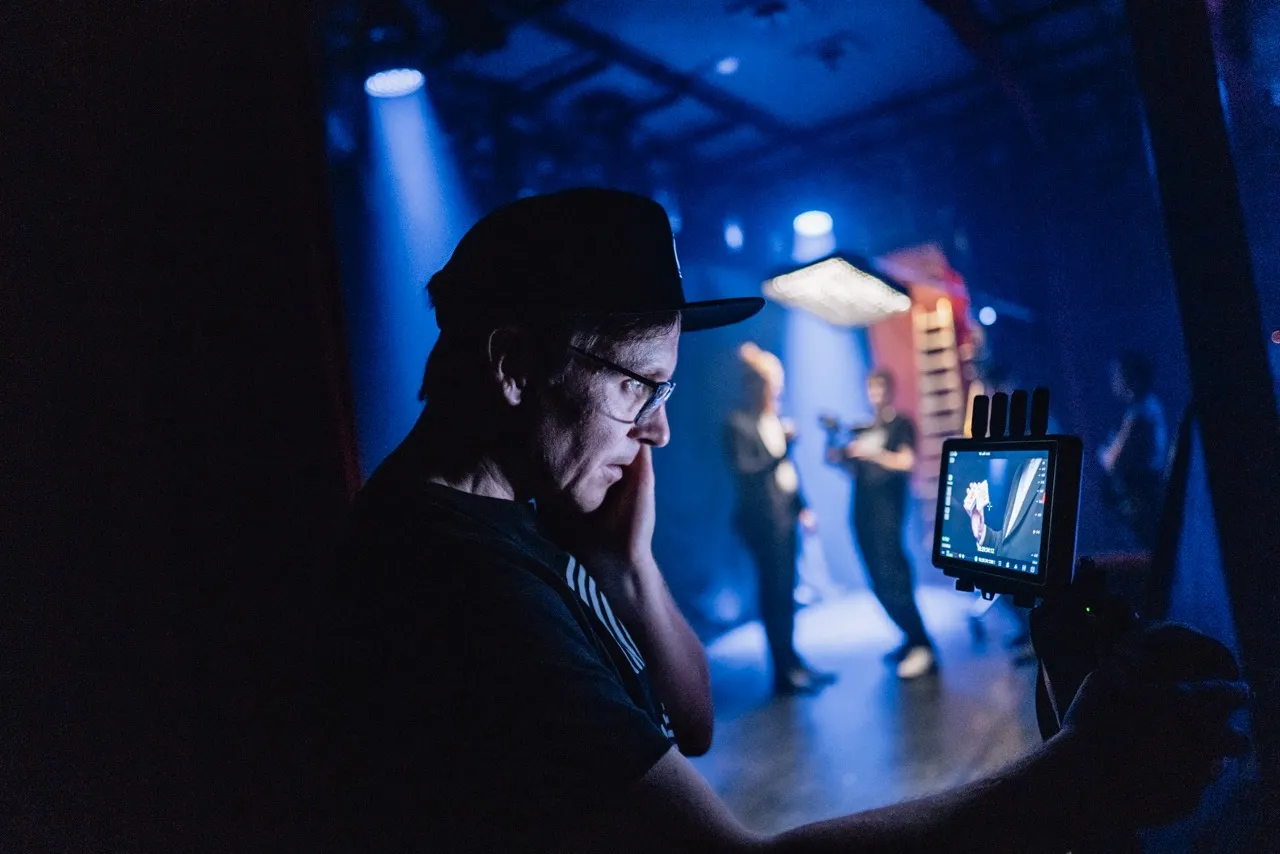 Auf einem Set für eine Filmproduktion in Hannover blickt der Regisseur auf einen Monitor. Im Hintergrund unscharf ist der Kameramann mit dem Protagonisten zu sehen.