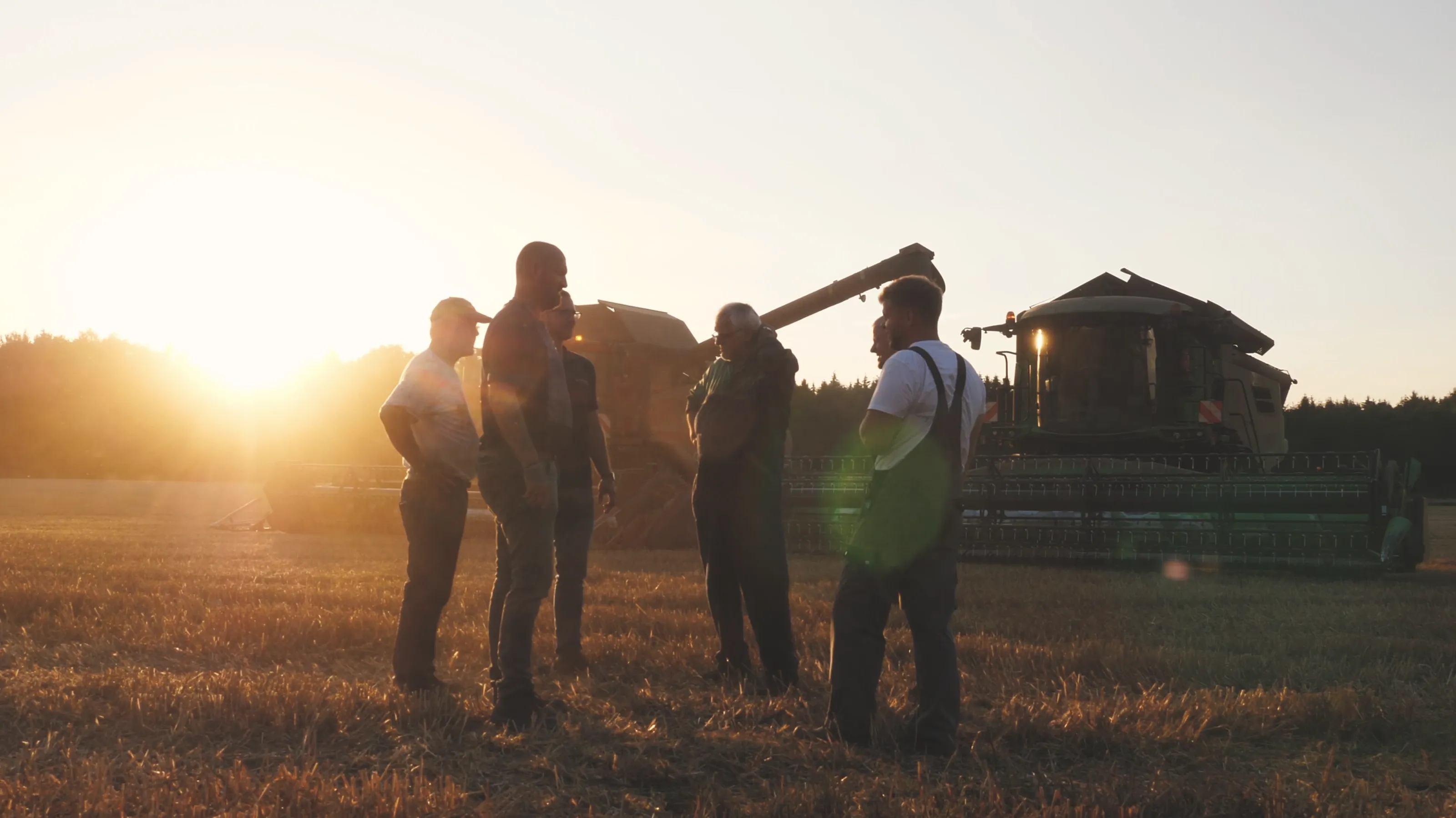 Eine Gruppe Bauern steht auf einem Feld bei Sonnenuntergang neben Erntemaschinen.